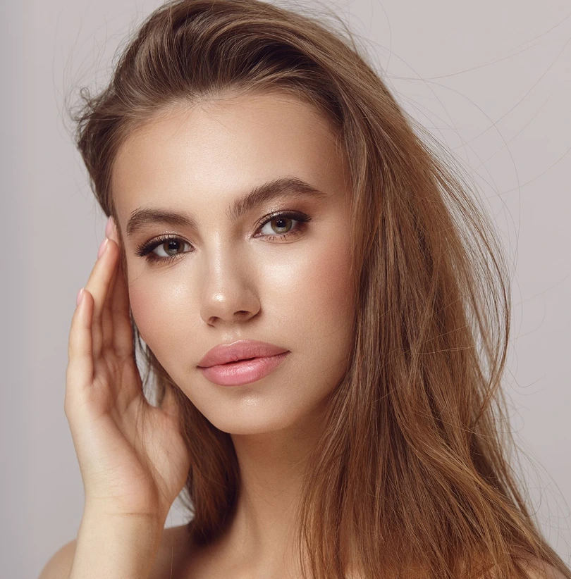 Woman with long brown hair touching her cheek, displaying refined facial features