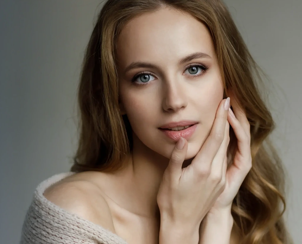 Woman with brown hair and blue eyes touching her face with both hands