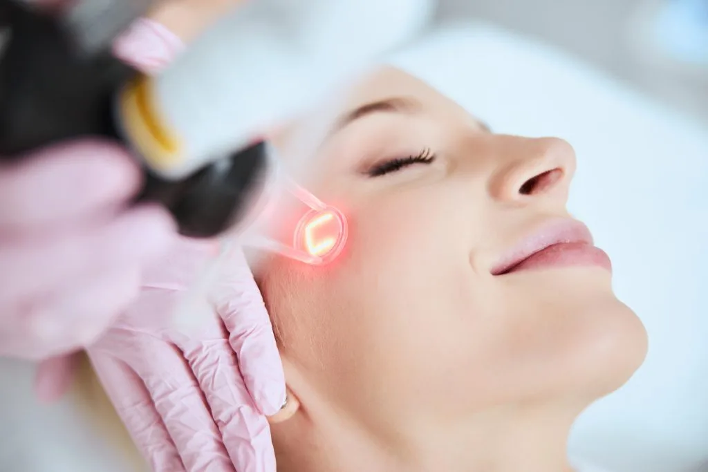 Provider using red-light therapy device on patient's cheek during facial treatment