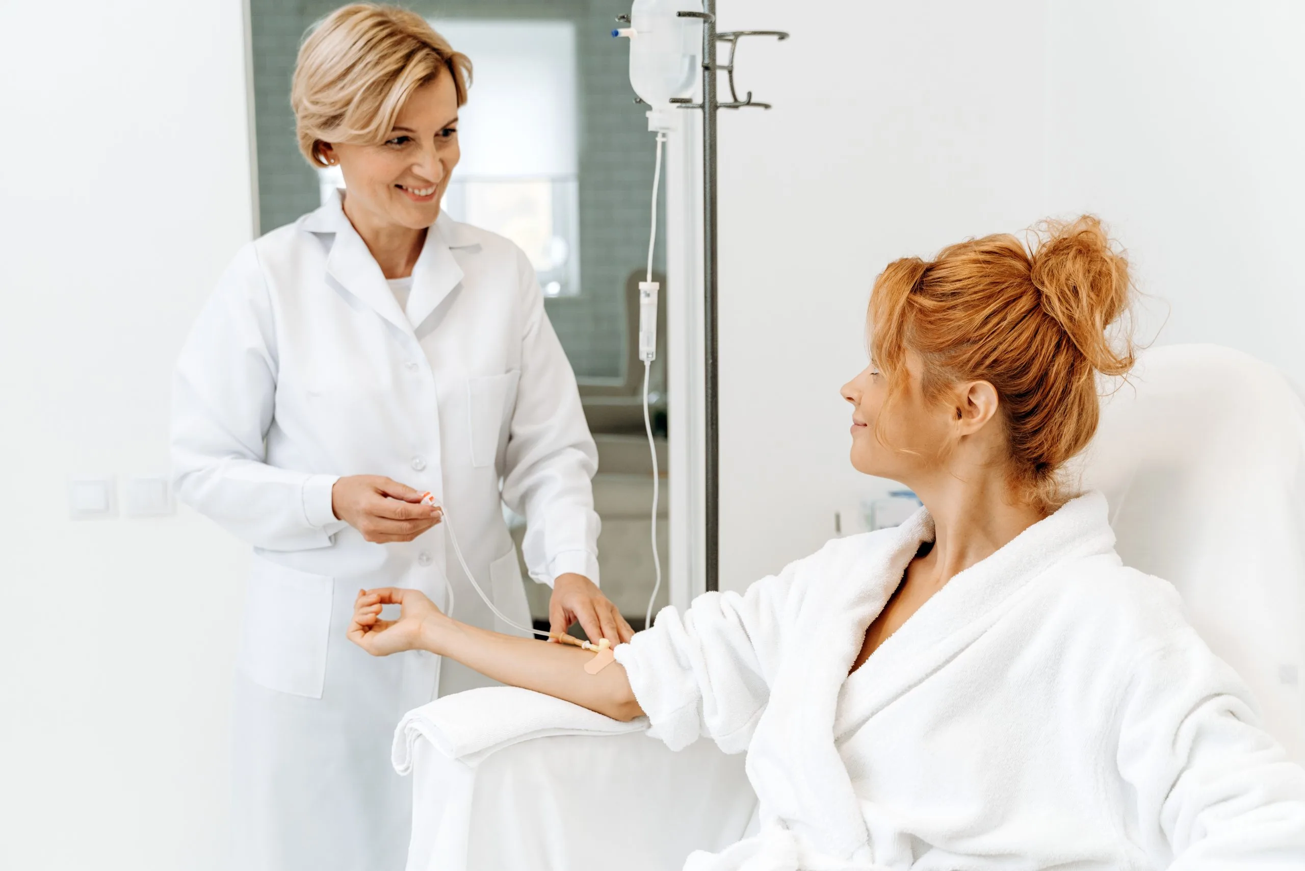 Healthcare provider in white coat consulting with patient in white robe near IV stand
