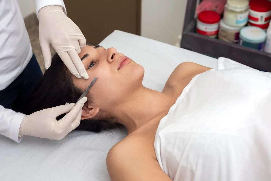 Esthetician applying product or performing a facial treatment on a patient's cheek and temple area