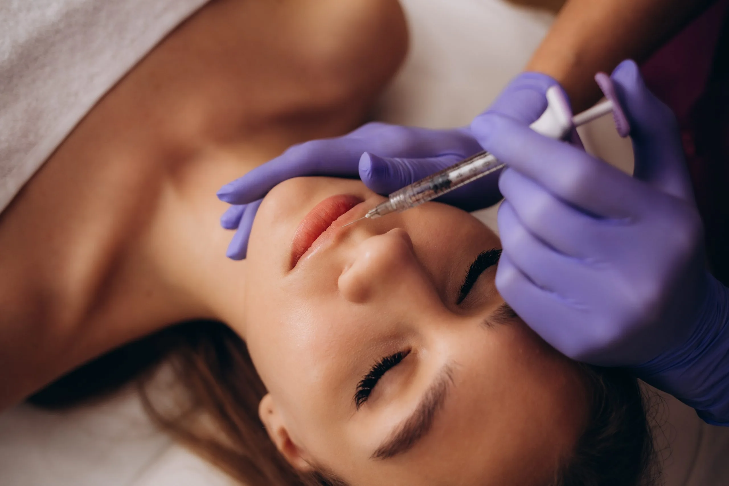 Practitioner in purple gloves injecting filler into patient's lips