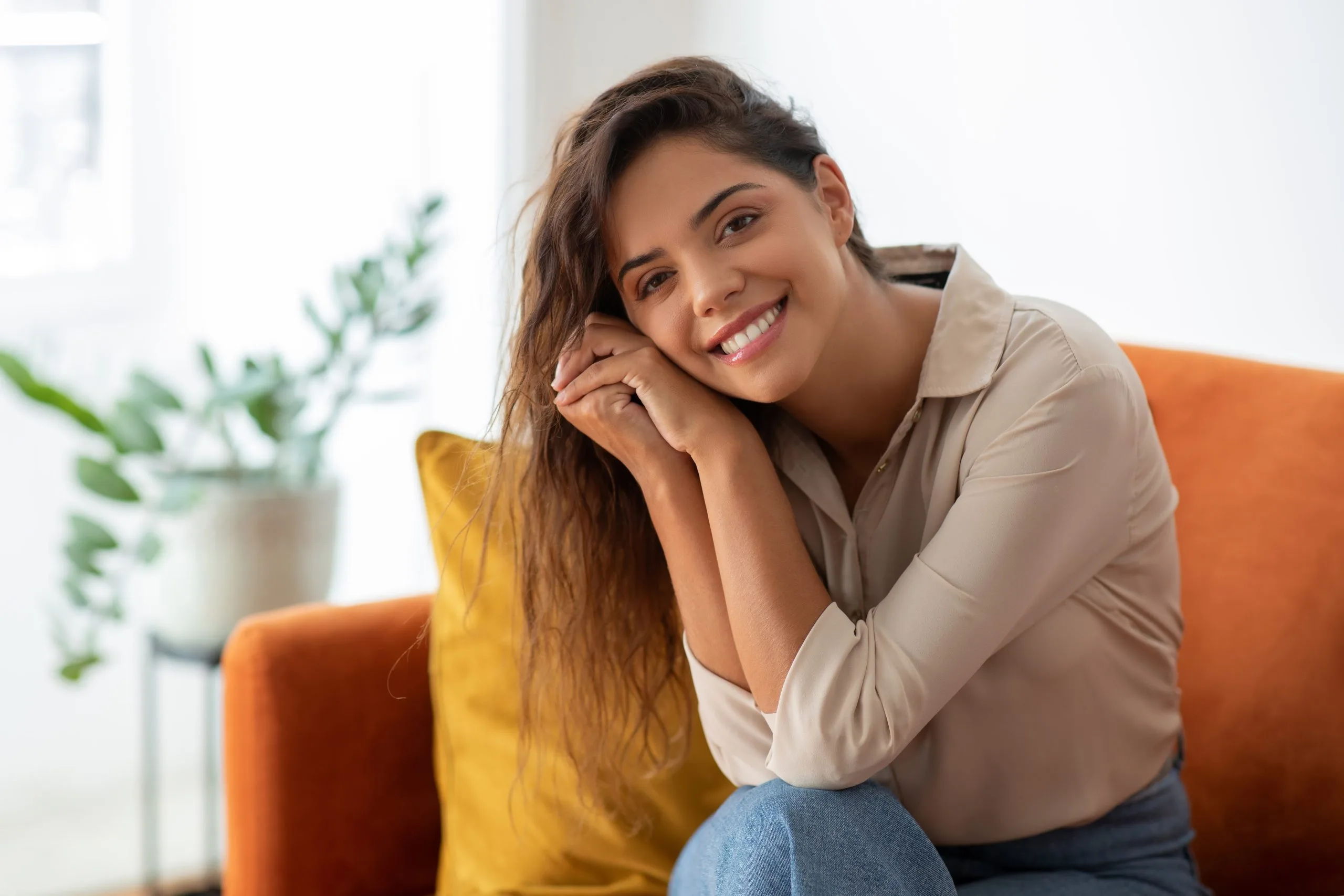 Woman smiling on orange couch with yellow pillow and potted plant