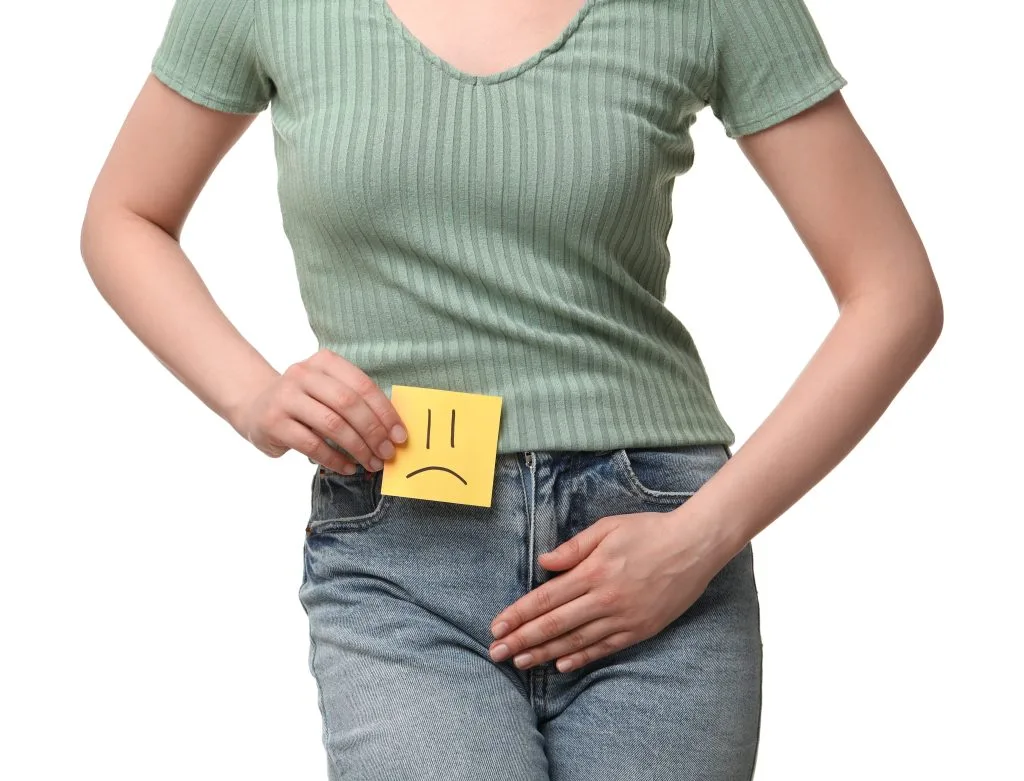 Person in green top holding yellow sticky note with sad face drawn on lower abdomen