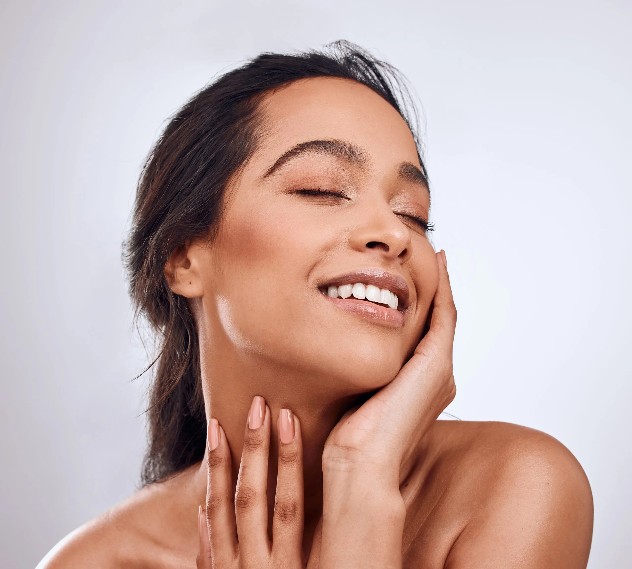 Woman touching her face with both hands, smiling with eyes closed