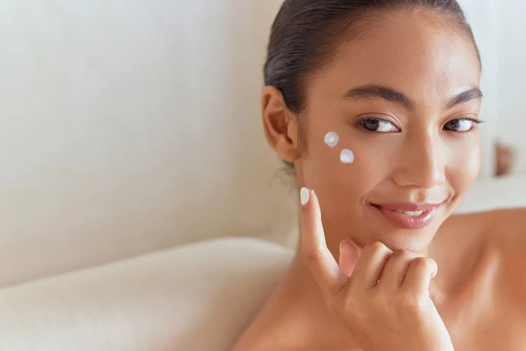 Woman pointing to skincare products on her cheek and forehead
