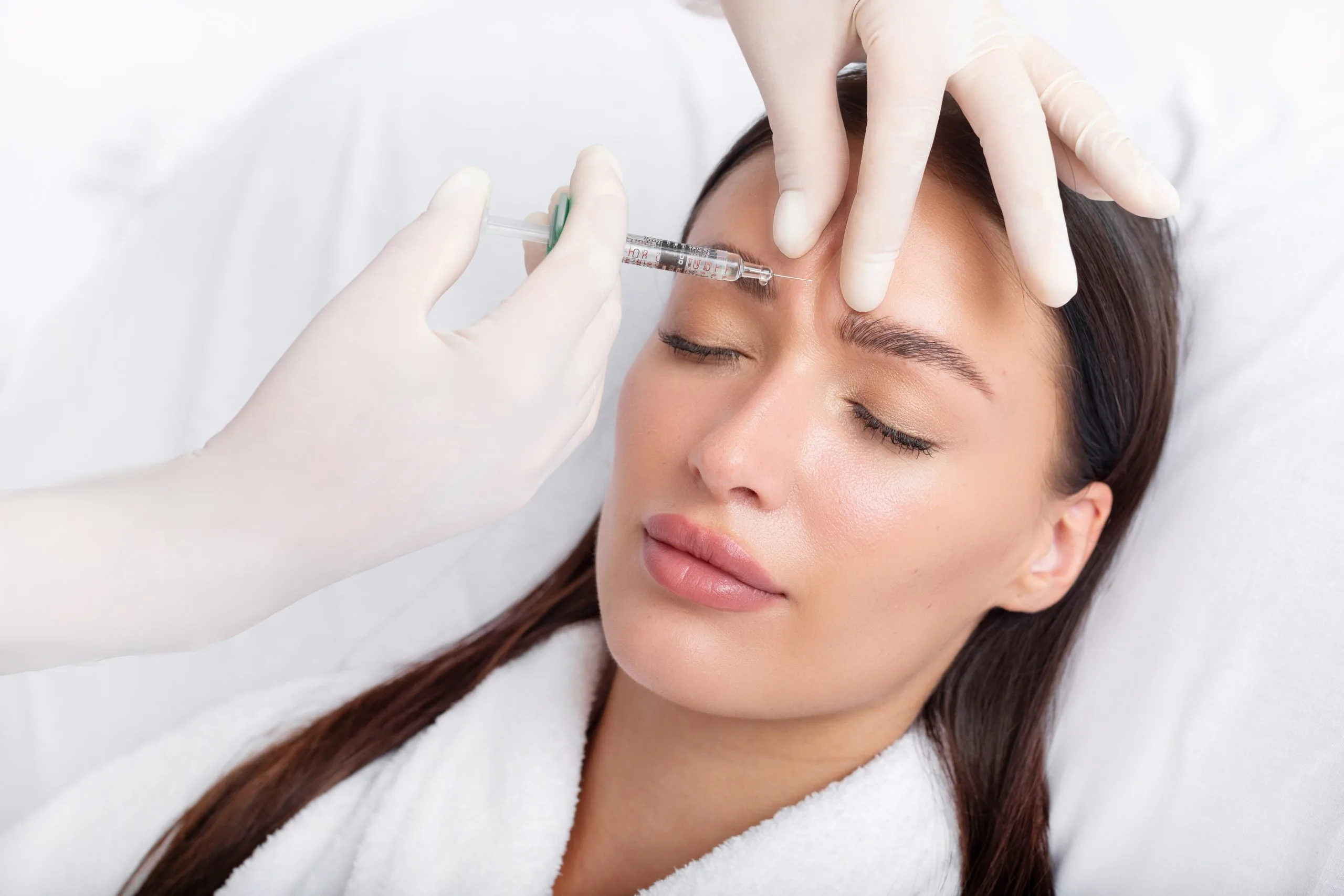 Clinician injecting filler into patient's forehead wrinkles with syringe