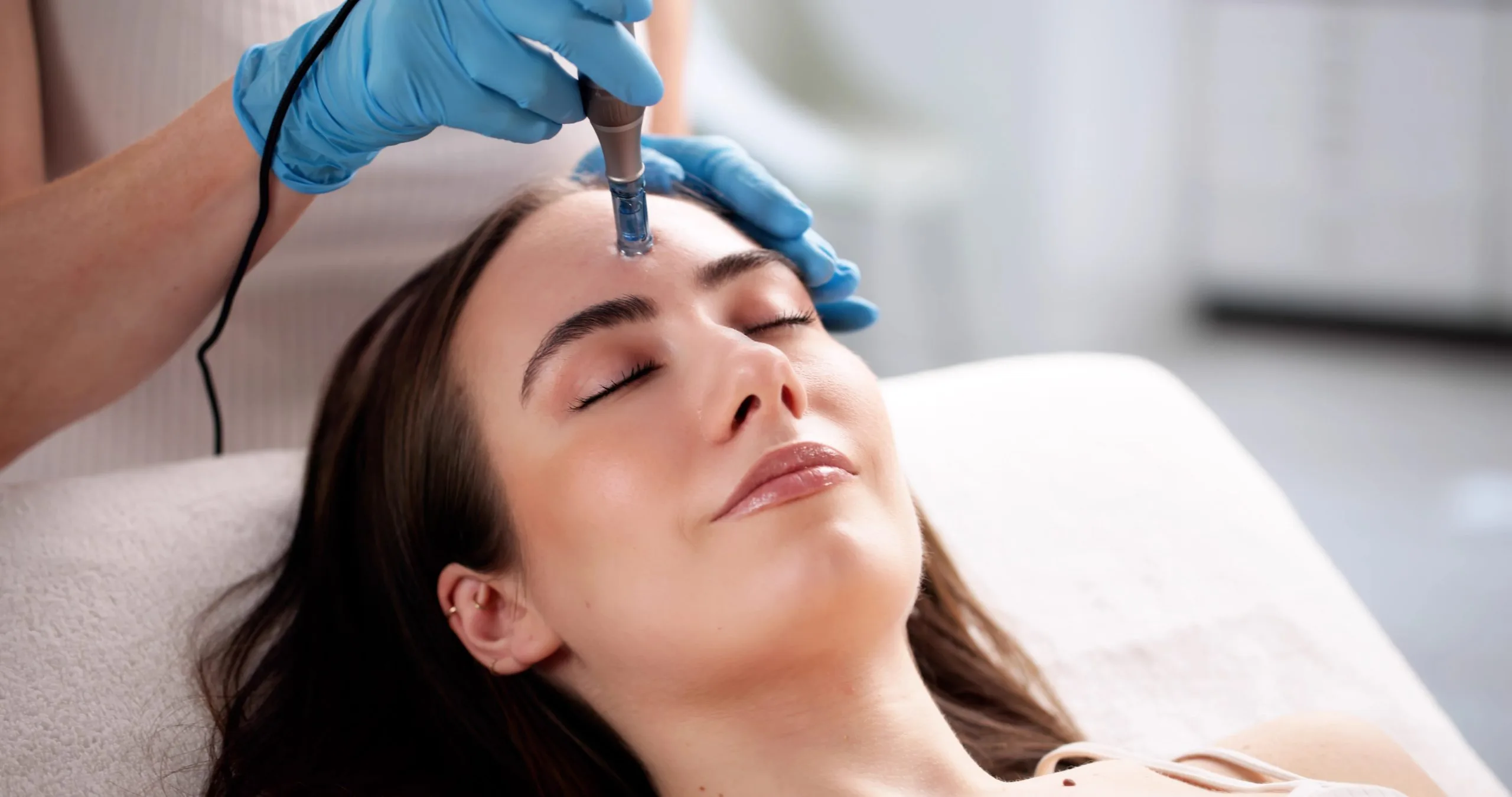 Practitioner in blue gloves using a handheld device on patient's forehead