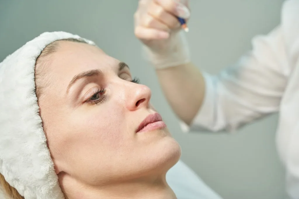 Provider applying a chemical peel or liquid treatment to a patient's face with a brush applicator