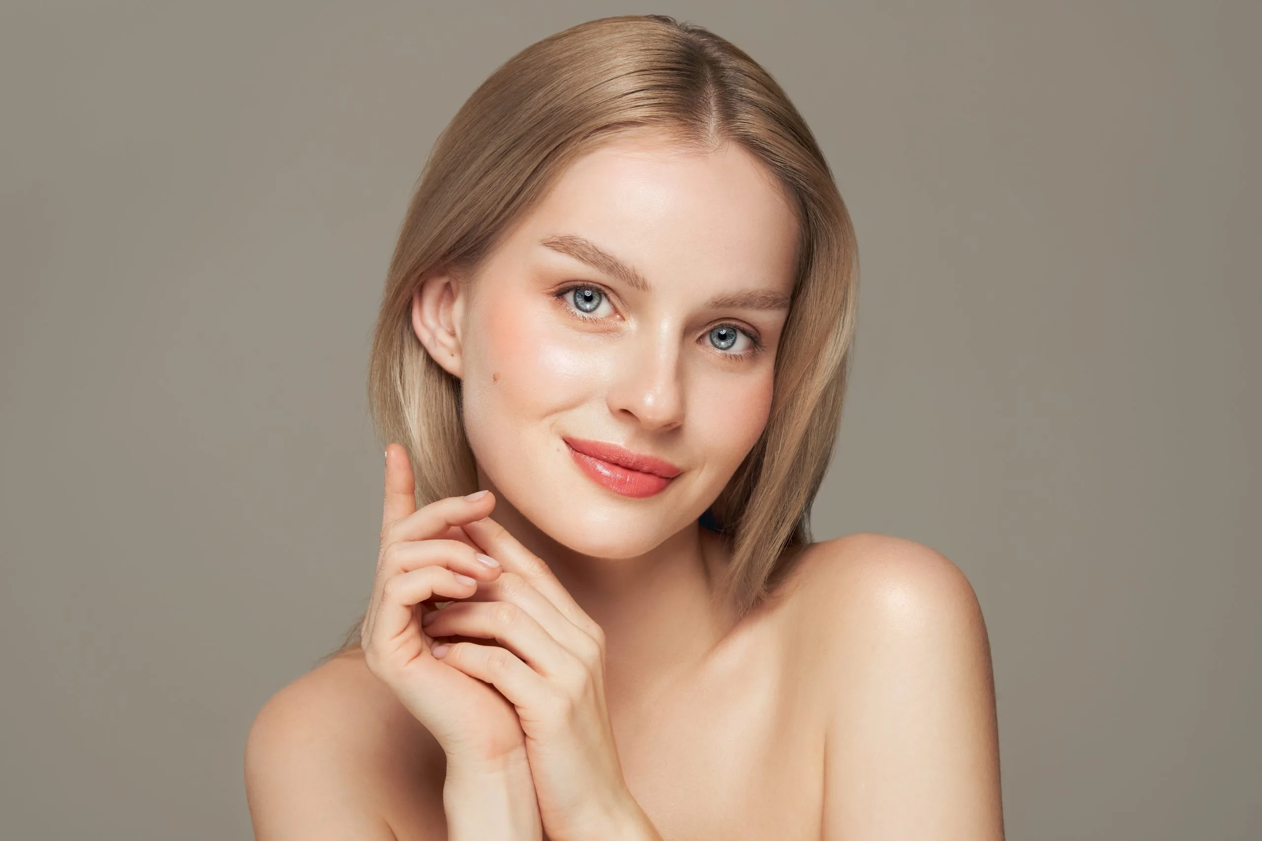 Woman with clear complexion and red lipstick touching her face against neutral background