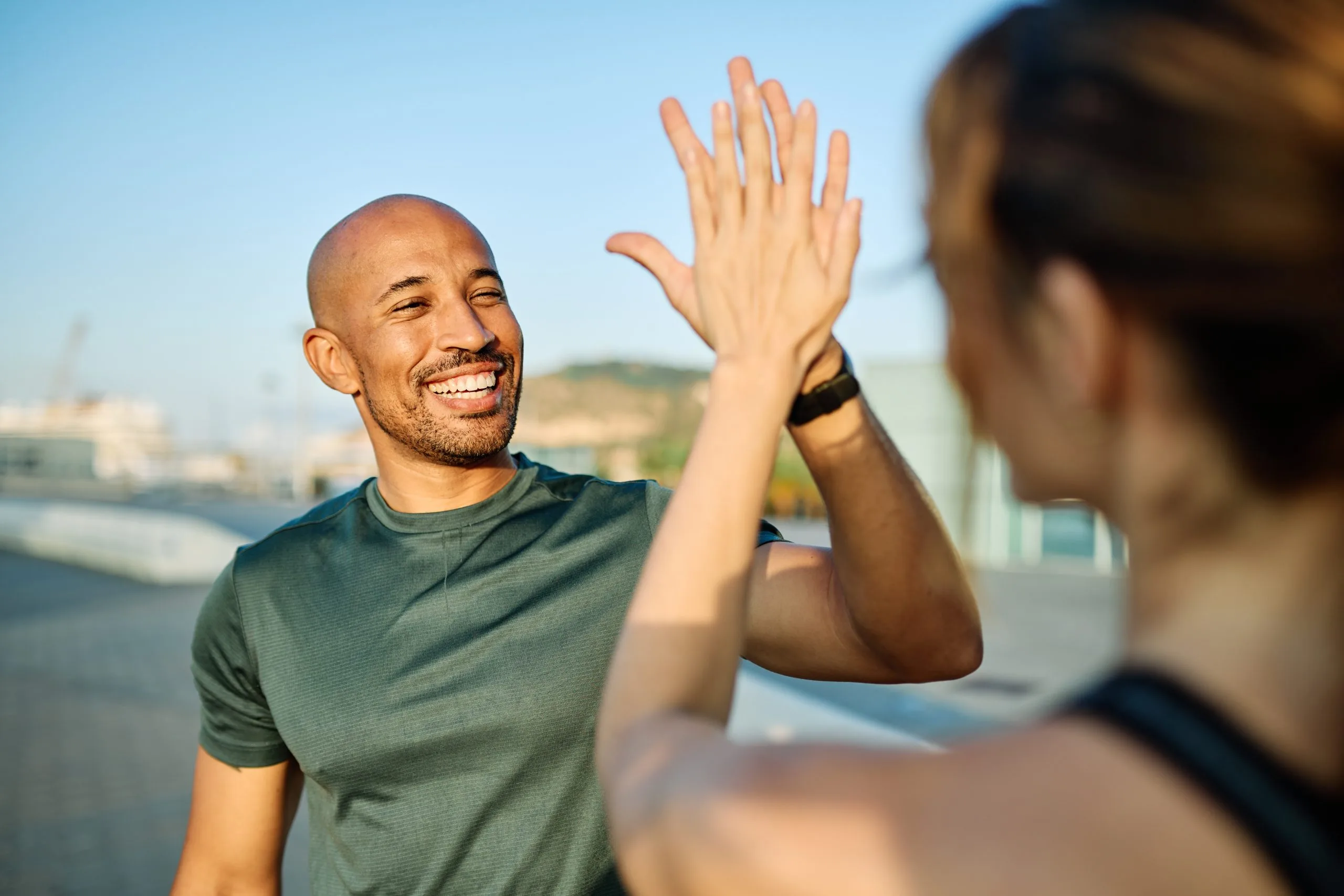 Two people high-fiving outdoors with waterfront in background