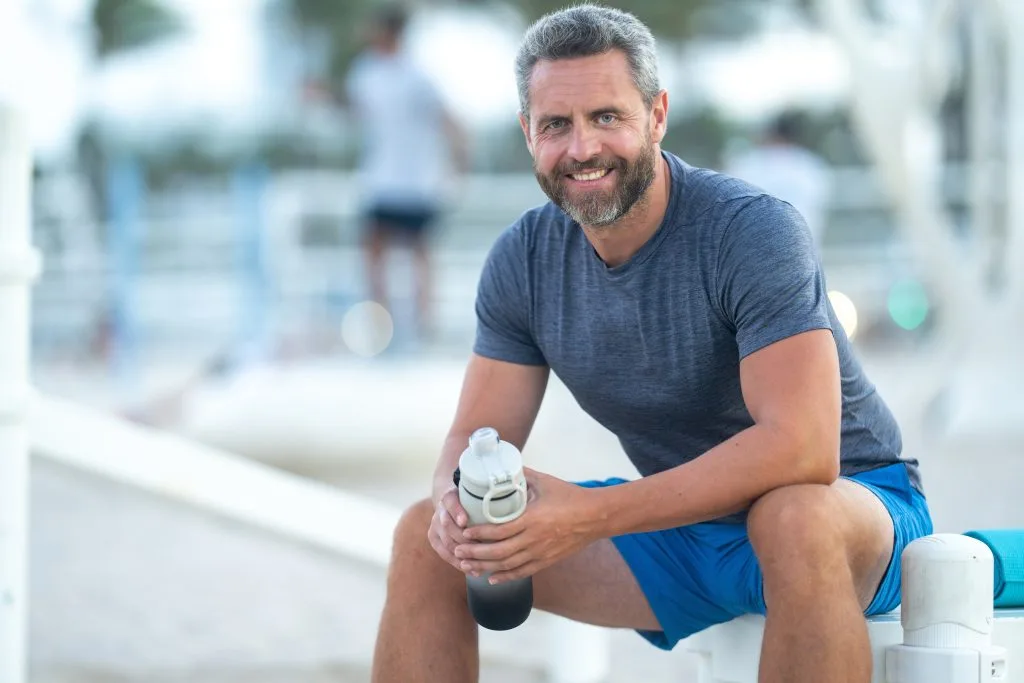 Man in blue shirt holding water bottle, smiling at camera outdoors