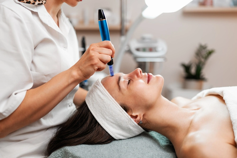 Cosmetologist performing microneedling with a dermapen device on a patient's face
